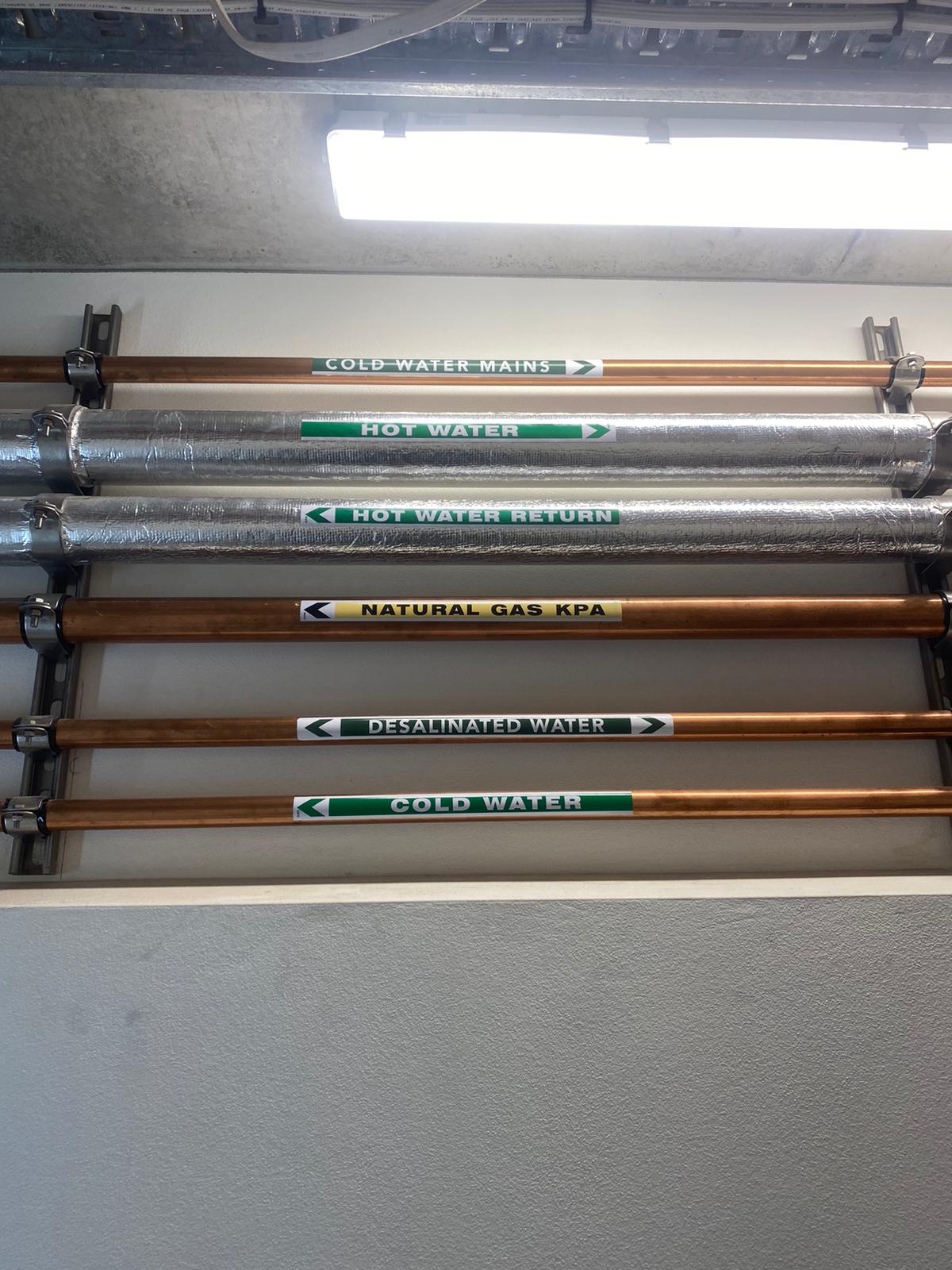 Six labeled pipes for Full Plumbing System Installations—cold water mains, hot water & gas—run along utility area
