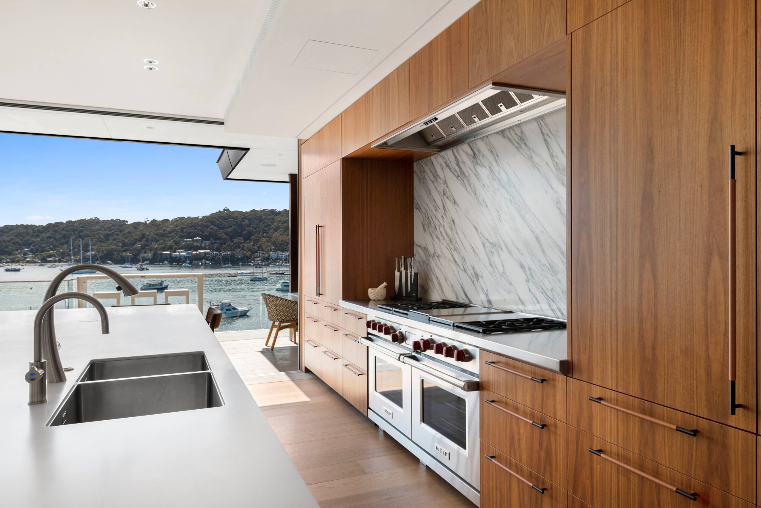 Modern kitchen with wood cabinetry, marble backsplash, island sink, and double oven featuring premium Kitchen Plumbing Design.