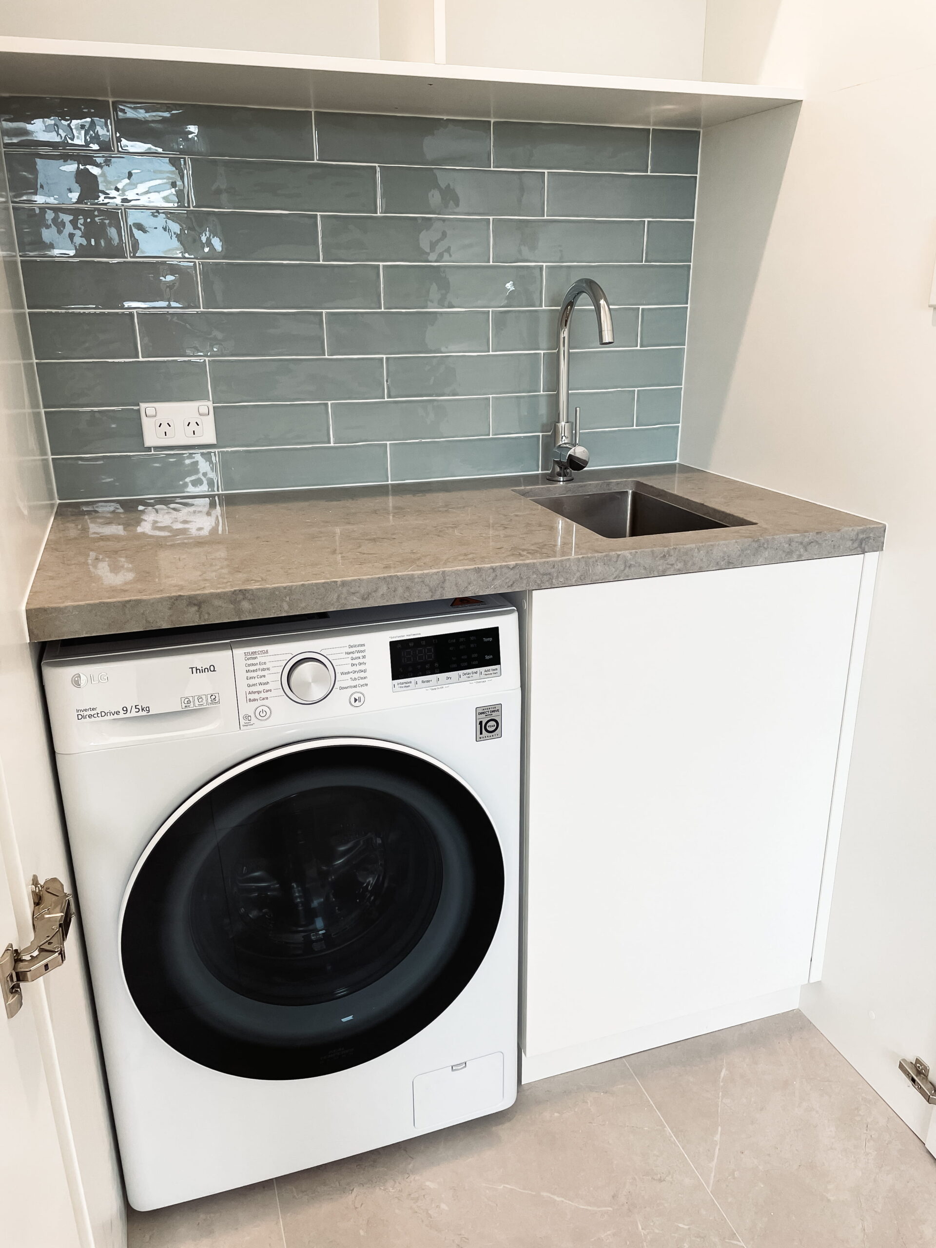 Modern Laundry & Utility Room with a front-loading washing machine, gray countertop, under-mount sink, and blue tile backsplash.