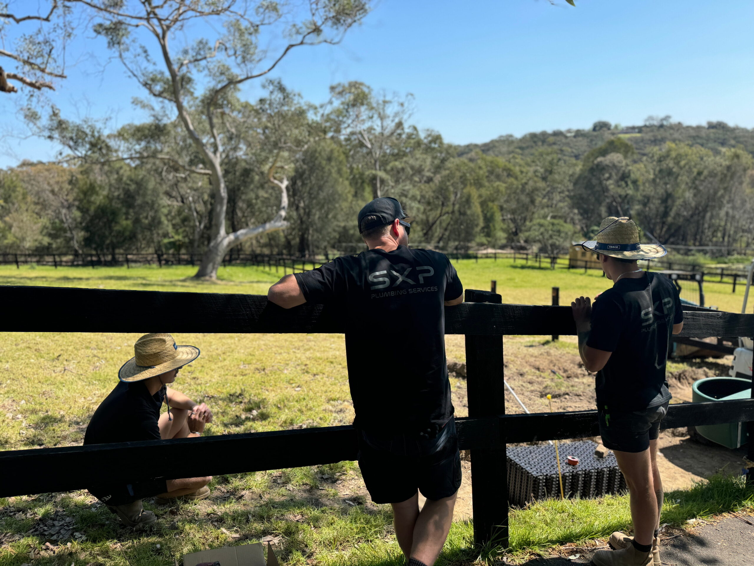 Three people in black shirts and hats pause by a fence, enjoying a sunny break during Start-to-Finish Project Management.