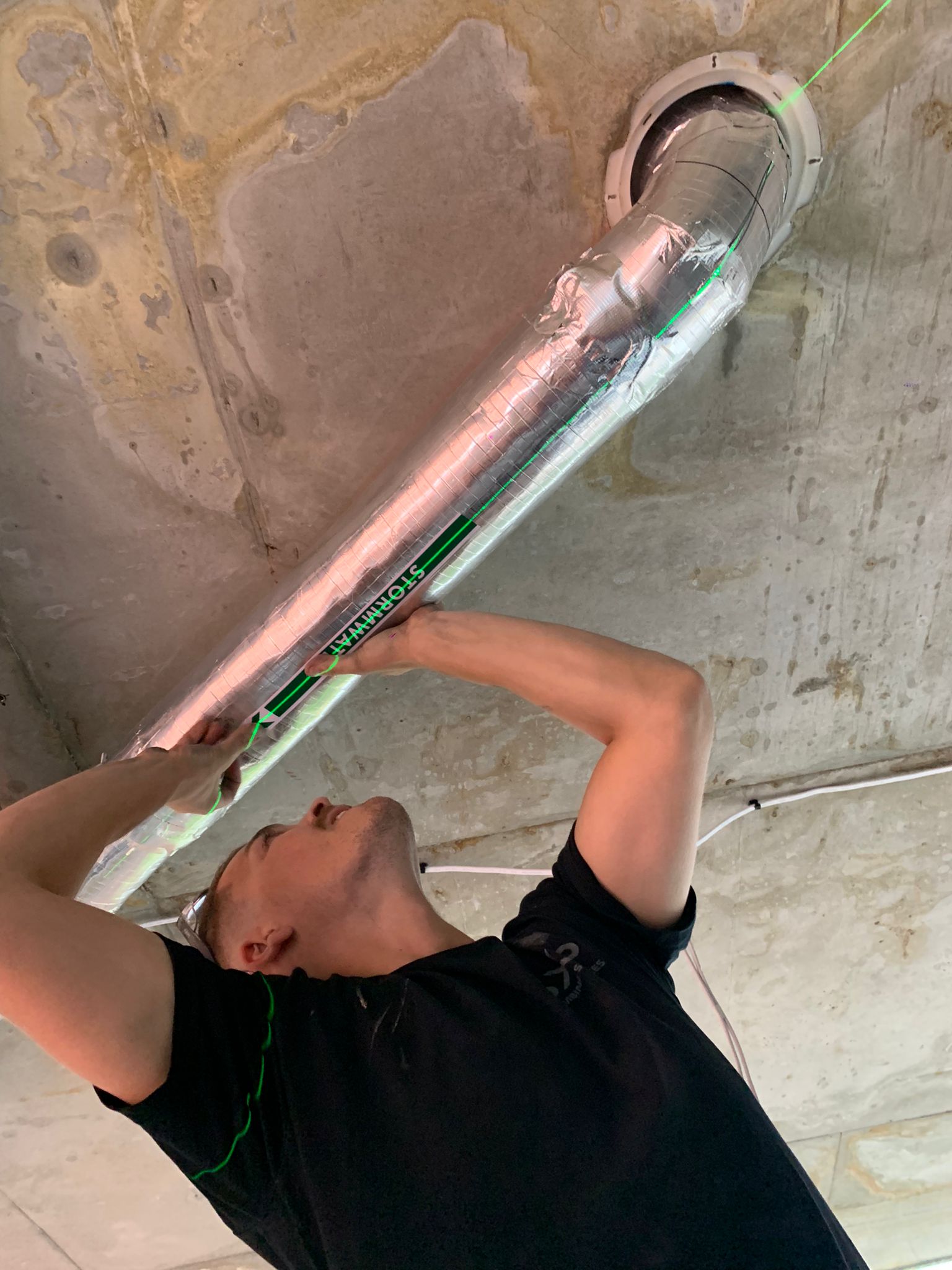 Inspects a silver duct on a concrete ceiling, showing expert Strata Plumbing Support.