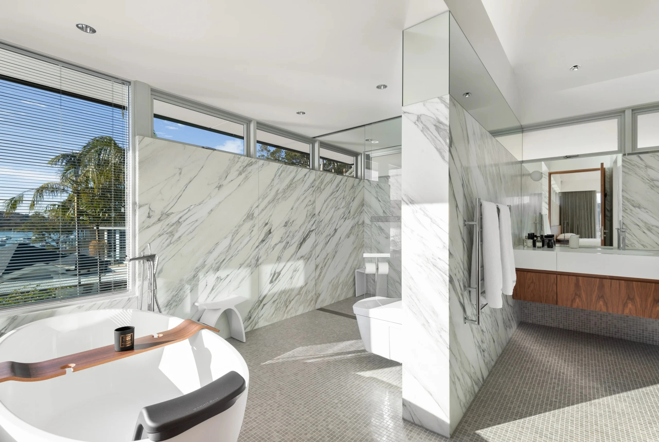 geotagged-Avalon-Project-02-scaled - SXP Plumbing - SXP Plumbing Bright, spa-like bathroom with marble walls, a curved freestanding tub in the foreground, and large windows letting in natural light.